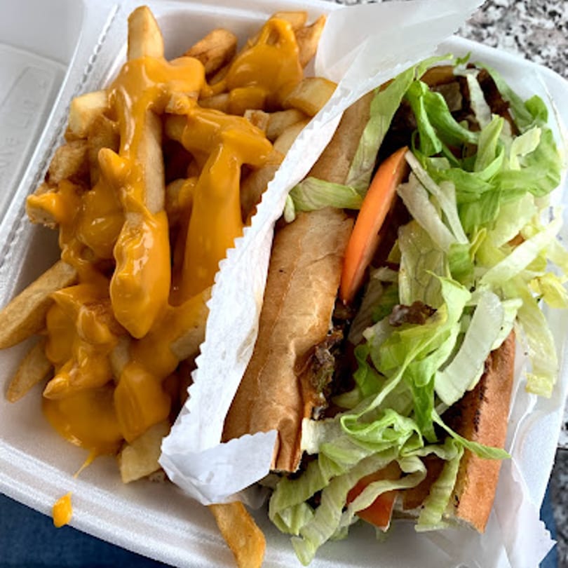 A Chicago Munchies cheesesteak sandwich with lettuce and tomato, next to cheese fries in a takeout container.